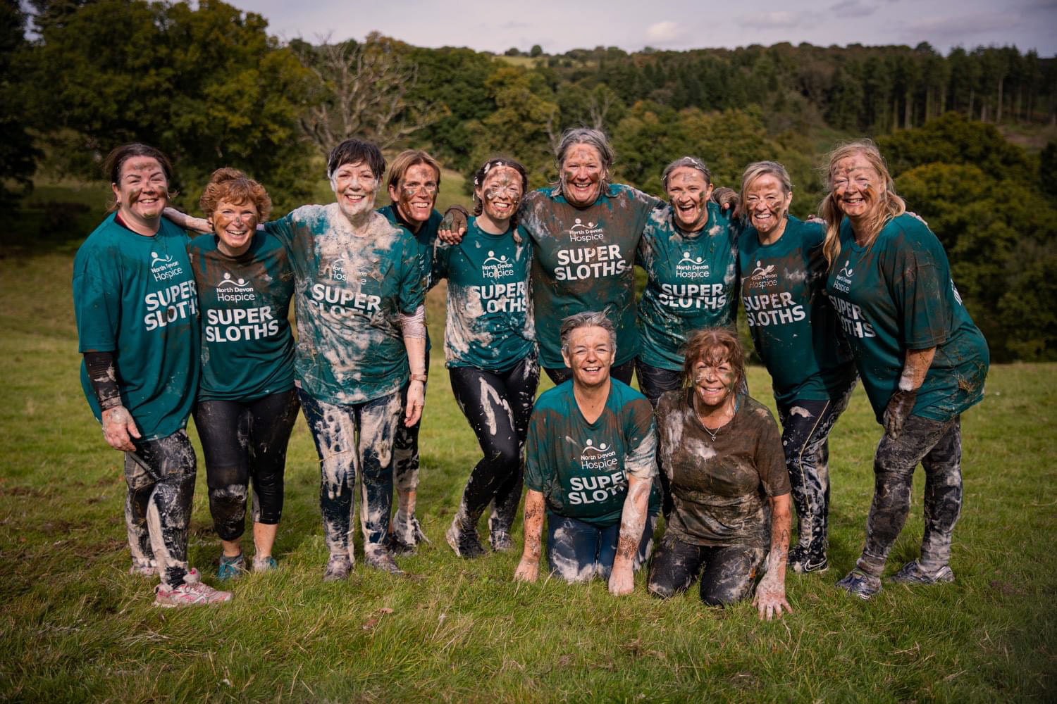 Team of females covered in mud and bubbles, having completed a commando course challenge, smiling to camera