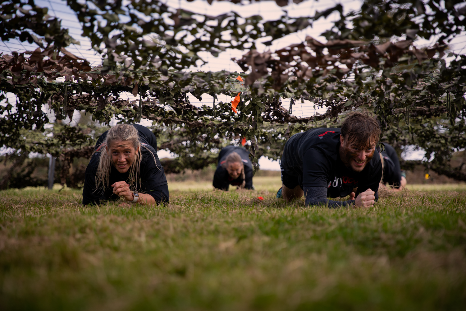 Female and male taking part in a commando style course, under netting crawling along the ground wearing face paint