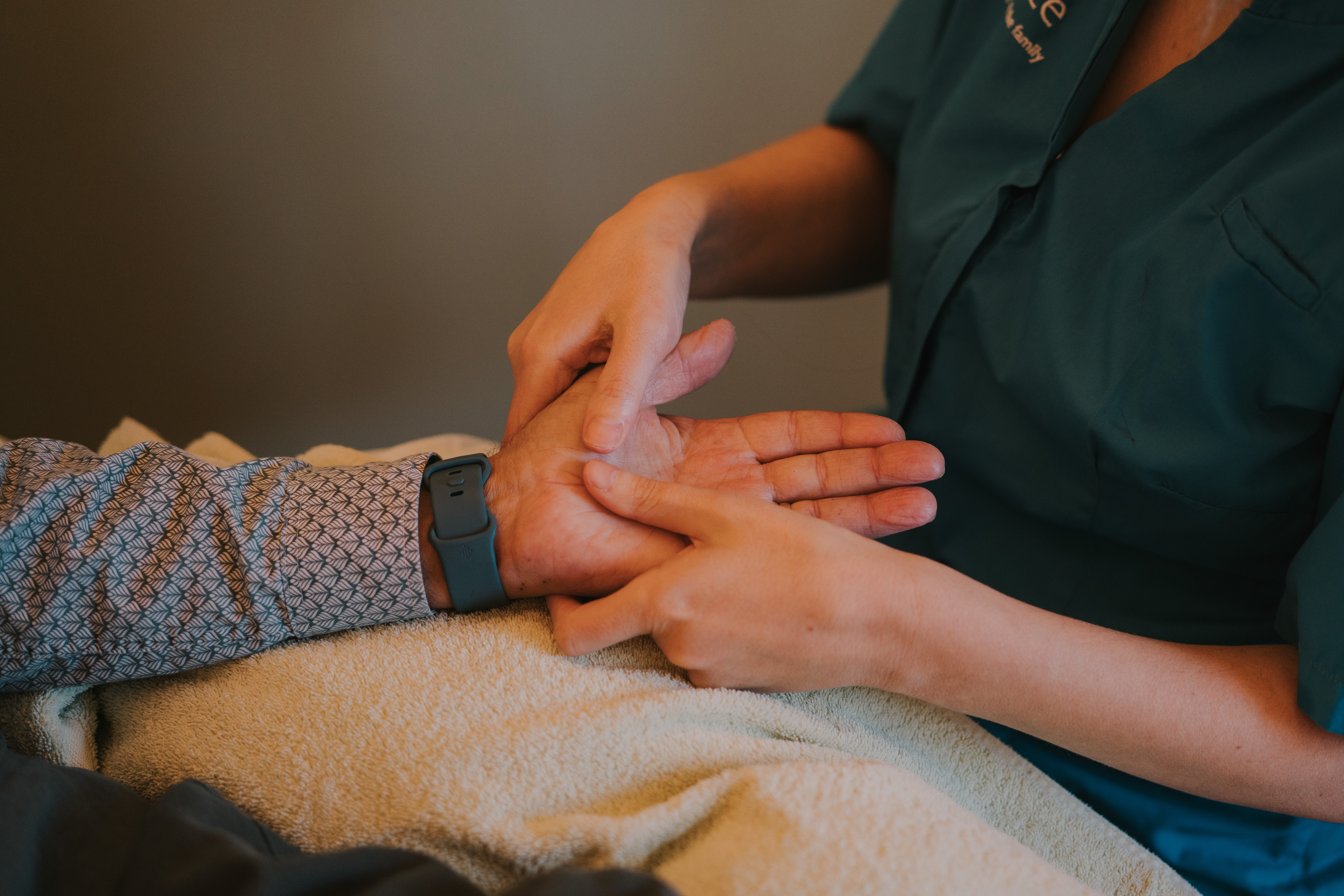 Female complementary therapist performing a hand massage on an elderly male patient with a cream towel underneath