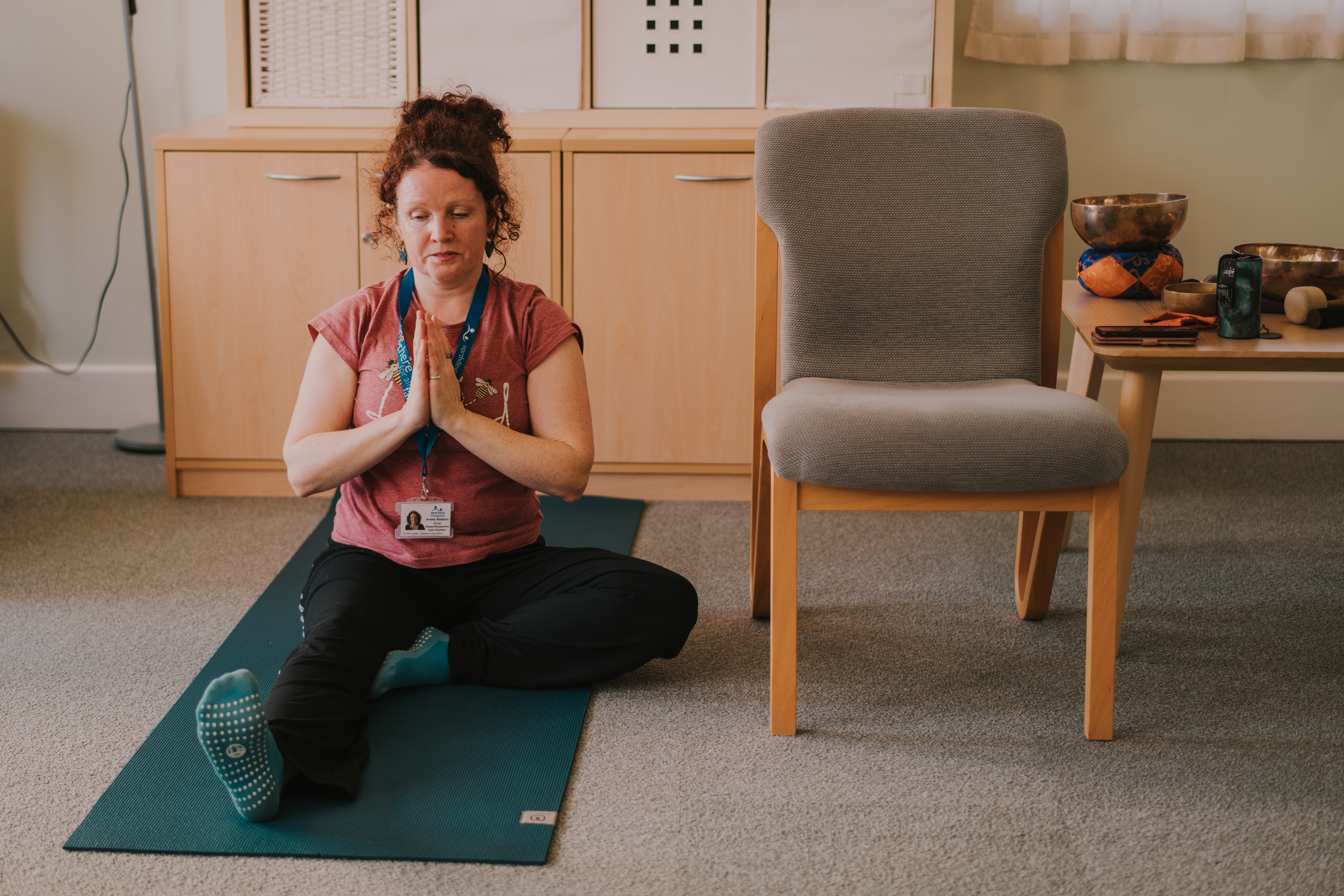 Female yoga instructor in a seated yoga pose on a green mat on the floor with her palms together